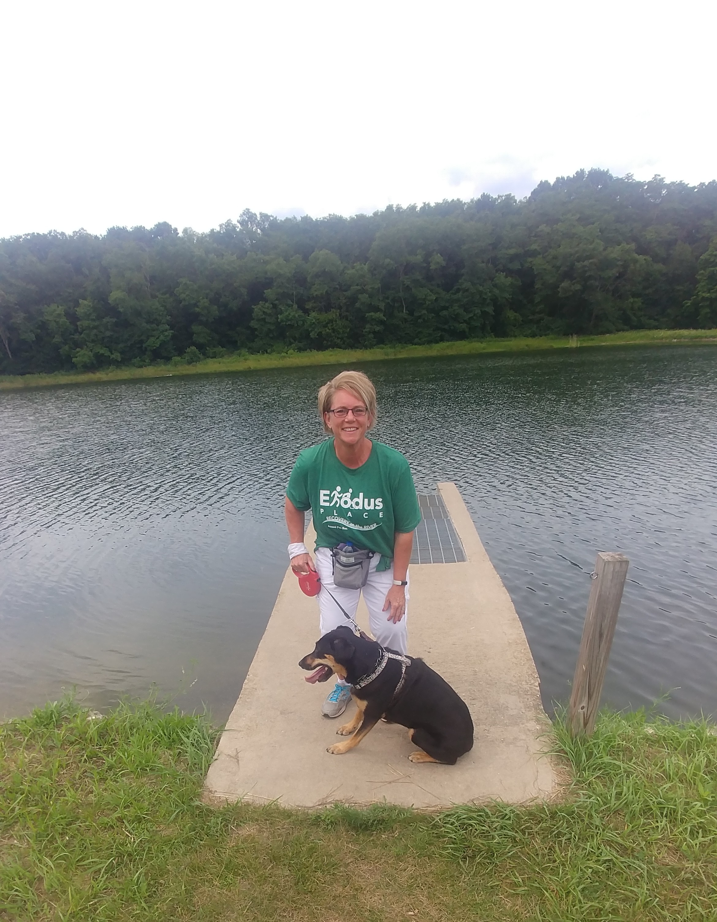 Bev Crandall-Rice participating in a virtual walk-a-thon with her dog, posing in front of a river